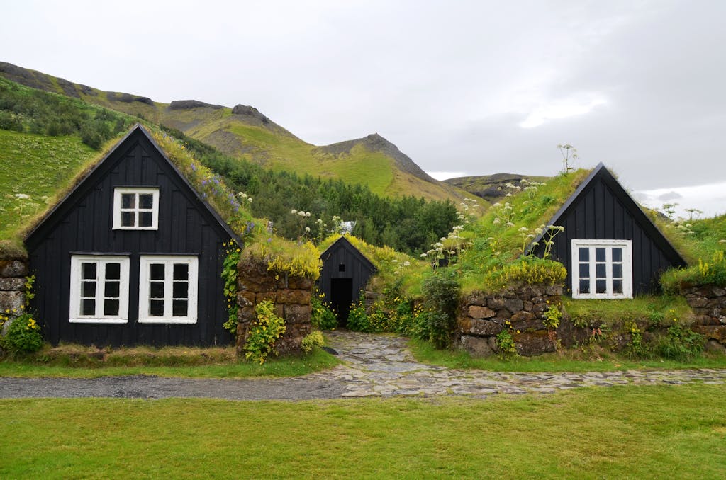 Explore the rustic charm of traditional turf roofed houses set against a lush hillside in serene countryside.