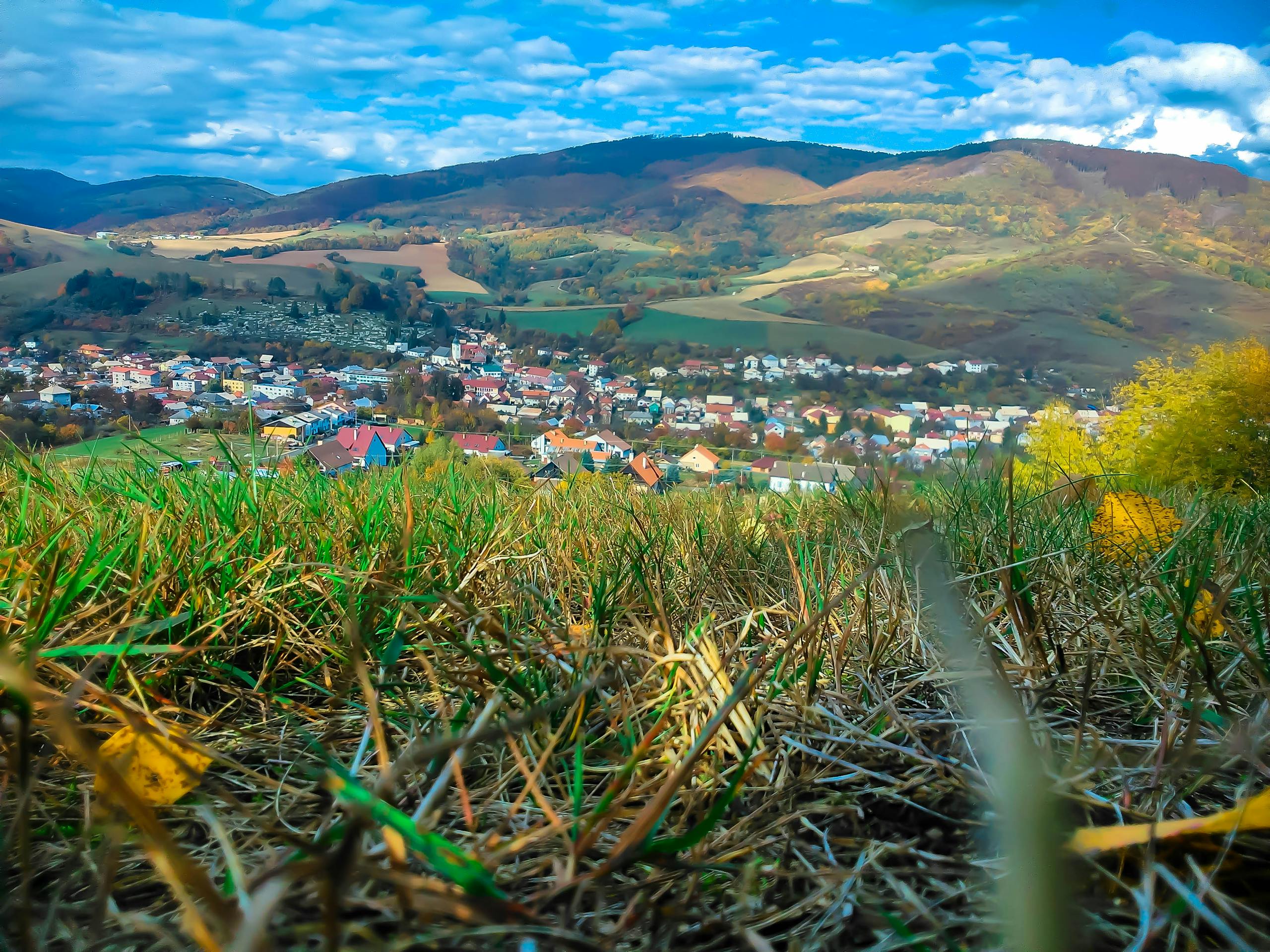 Serene view of a quaint village nestled within lush rolling hills and vibrant grass, bathed in daylight.